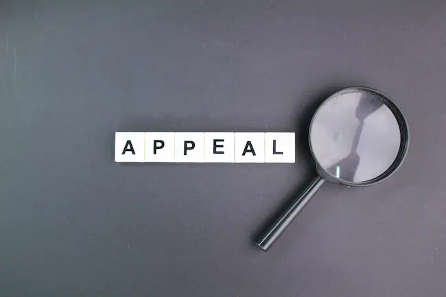 A magnifying glass examining a word appeal representing long-running appeals processes and extended litigation challenges for injury victims.