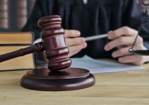 A judge in a black robe reviews documents and holds a pen beside a wooden gavel on the bench representing the judicial process involved in cases where attorneys help clients identify and challenge a record trap in California.