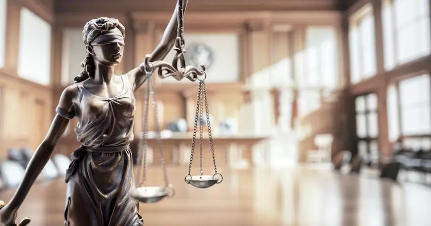 The blindfolded Lady Justice statue is holding balanced scales is standing inside a courtroom symbolizing the impartial pursuit of justice for clients seeking legal help to overcome a record trap in California.